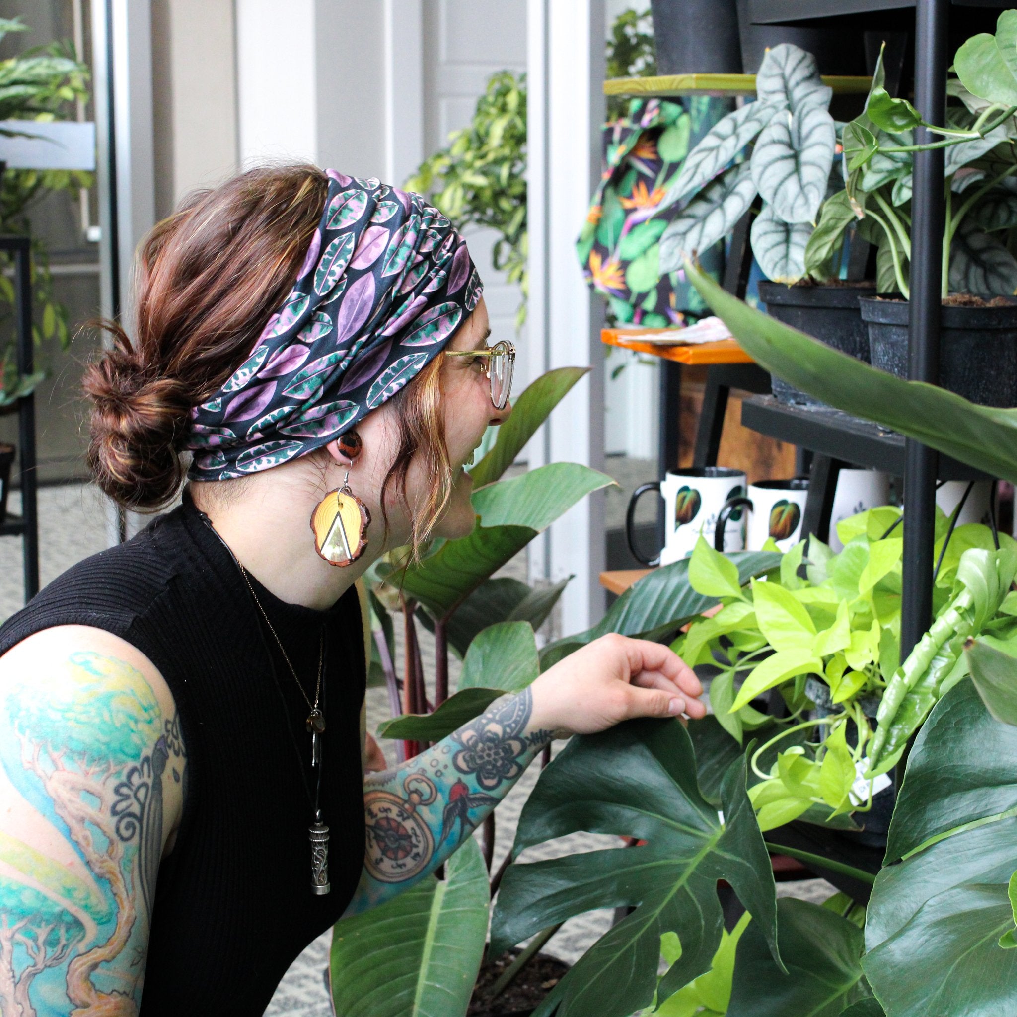 Person with tattoos tending to plants in a greenhouse.