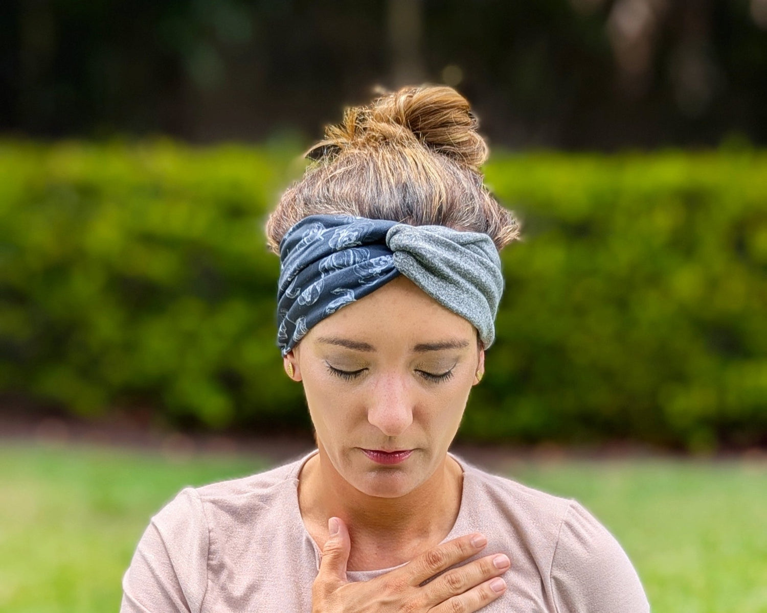 Woman wearing a blue headband outdoors with greenery in the background