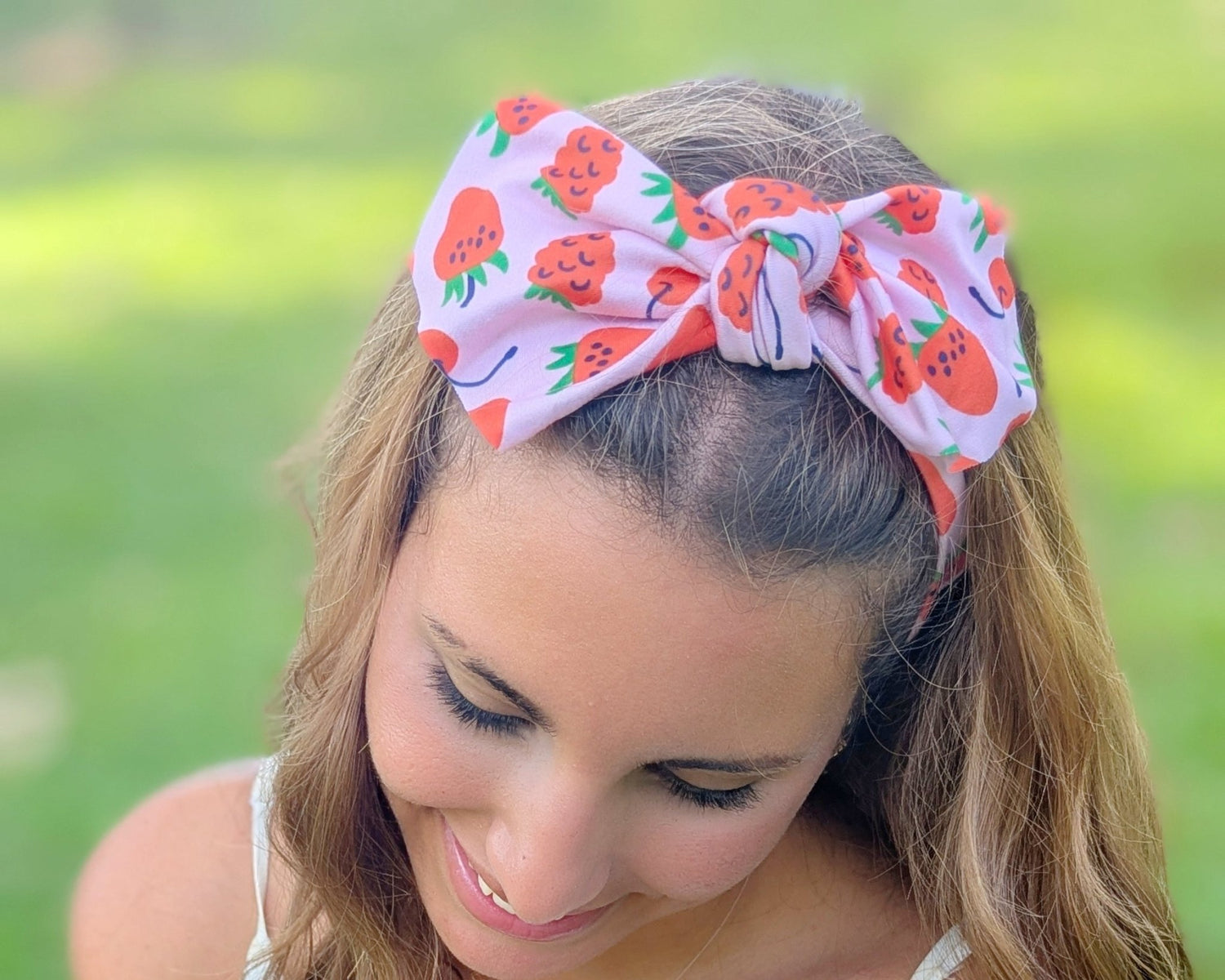 Woman holding strawberries wearing a floral headband in a grassy outdoor setting