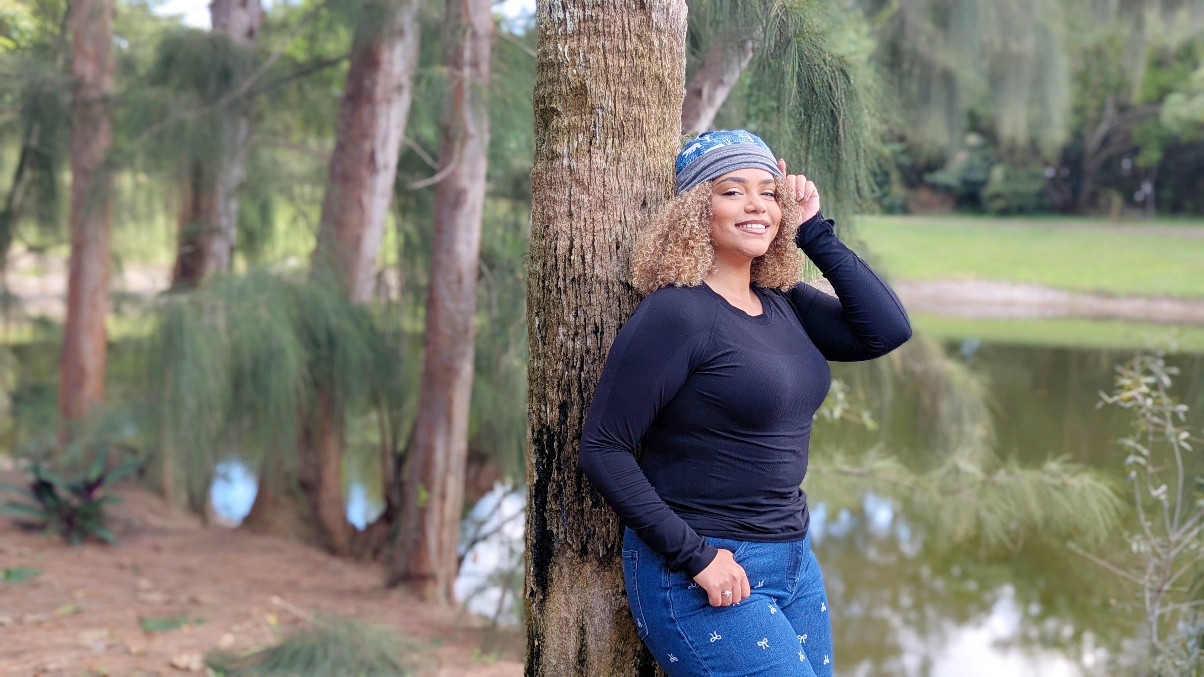 Woman in a blue outfit standing next to a tree by a pond in a park