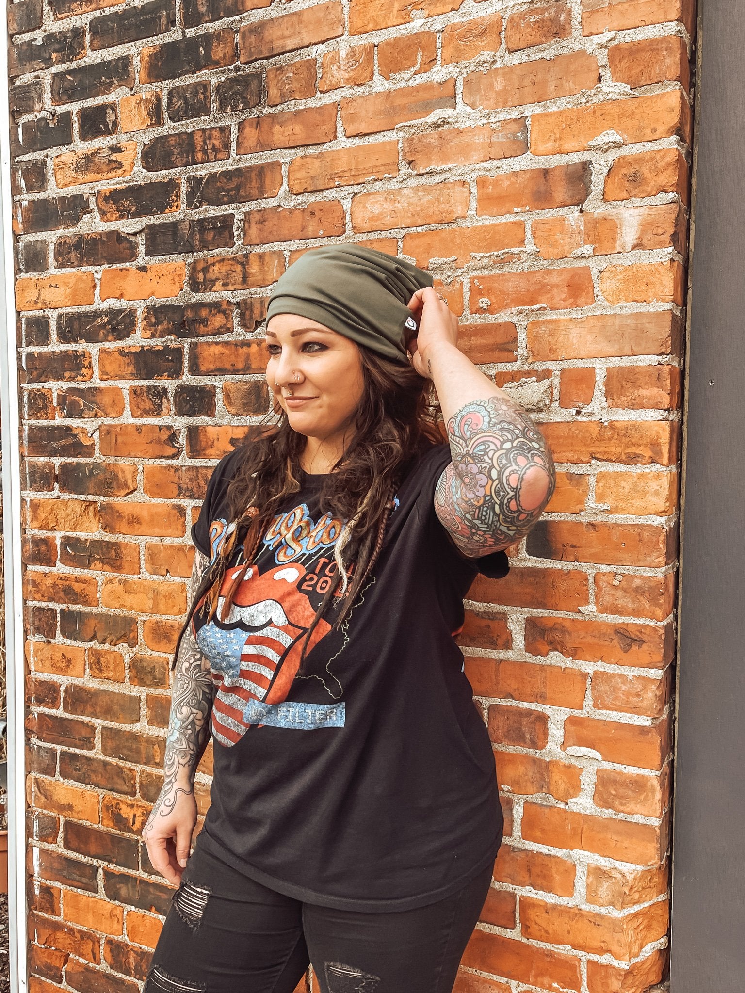 Person wearing a black t-shirt with a graphic design, standing against a brick wall.