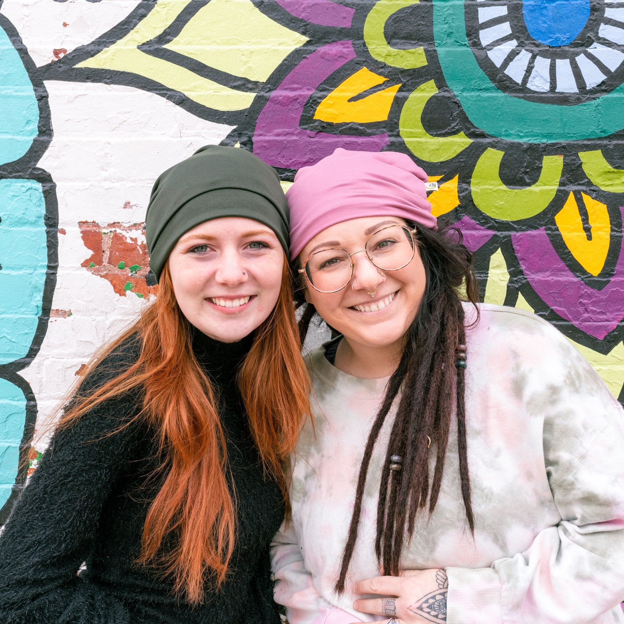 Two women wearing headscarves standing in front of a colorful mural.