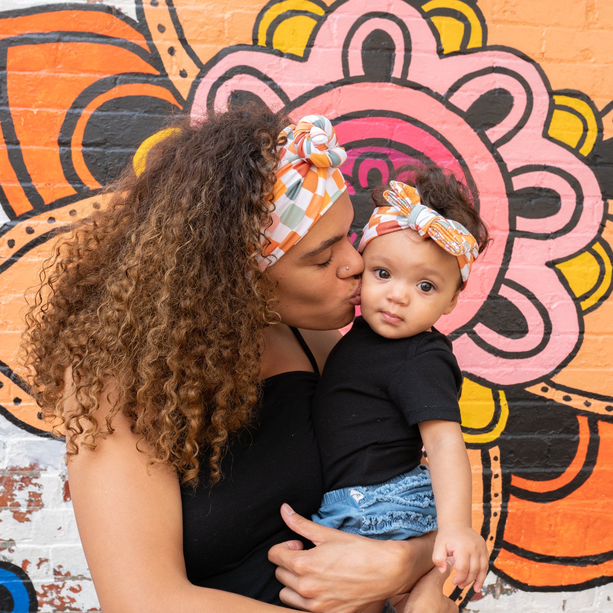Woman kissing baby on the cheek against a colorful mural background