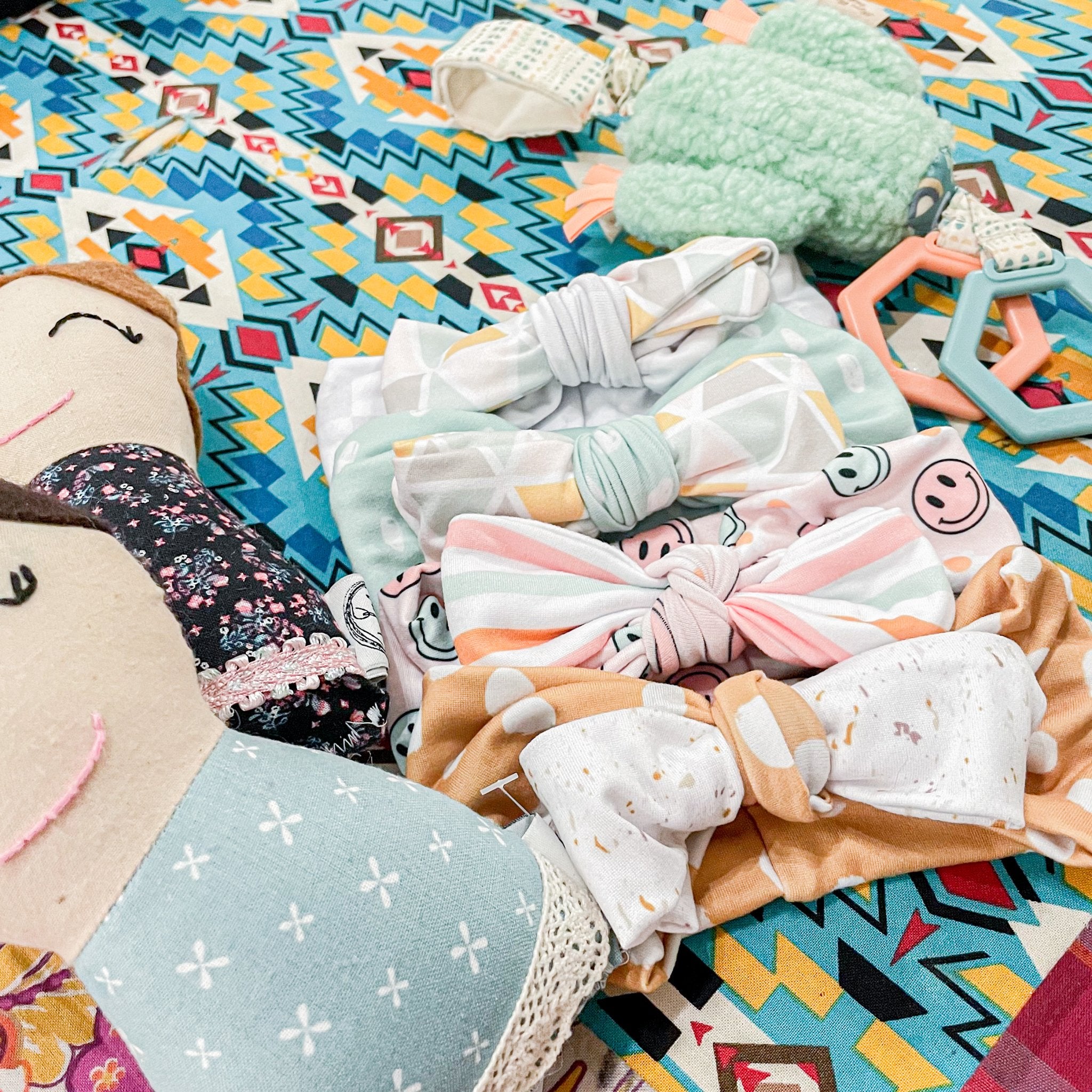 Colorful baby accessories including headbands and a plush toy on a patterned surface.