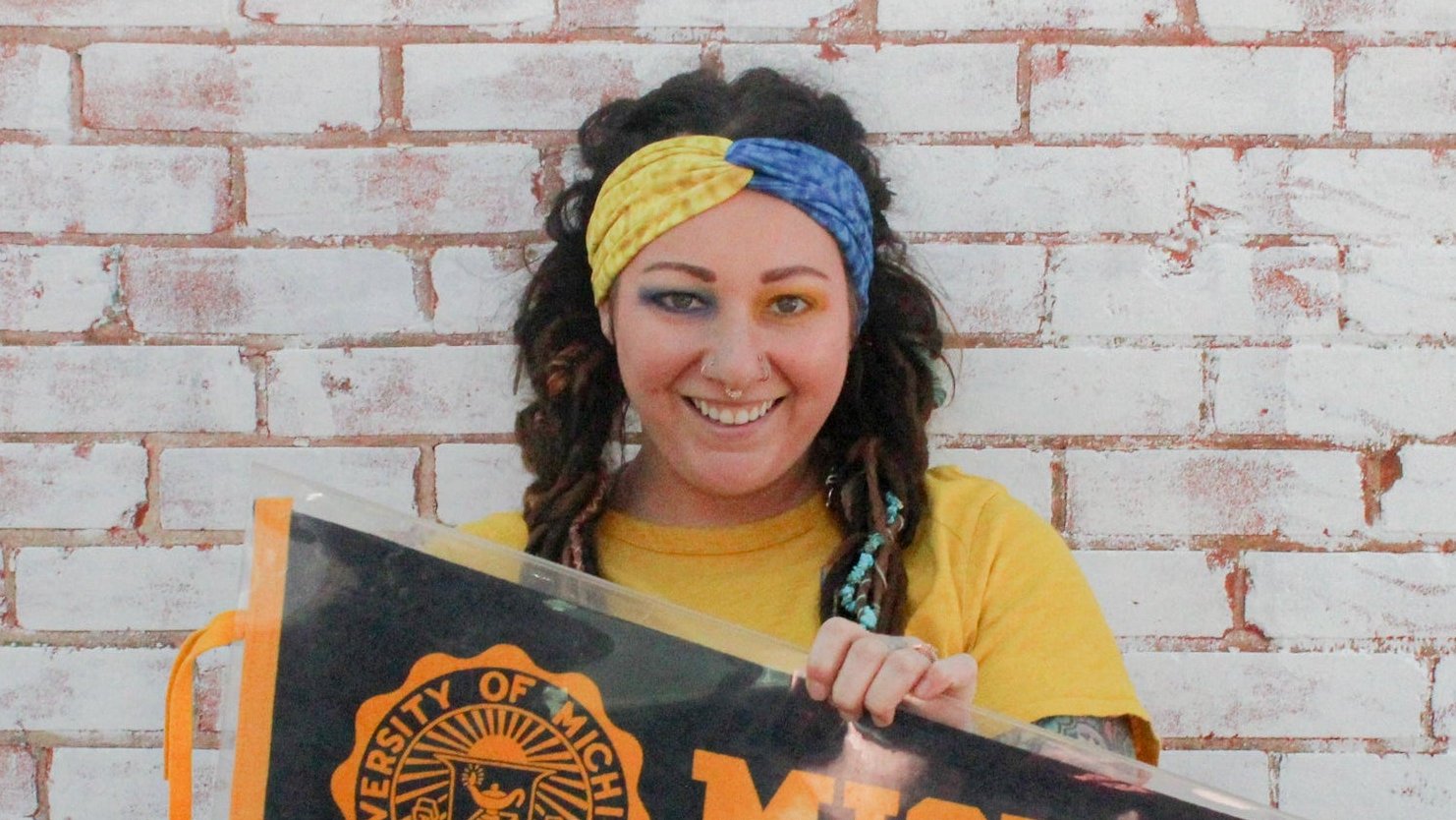 Person holding a sign with 'University of Michigan' text against a brick wall.