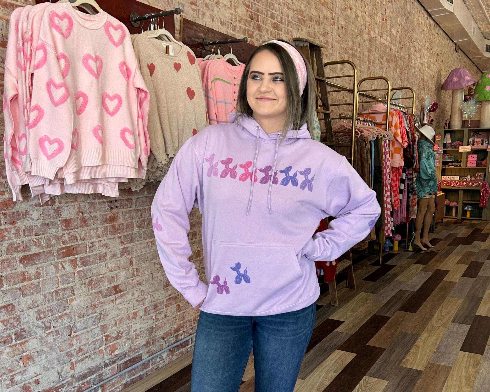 Woman wearing a light purple hoodie with colorful text and graphics in a clothing store.