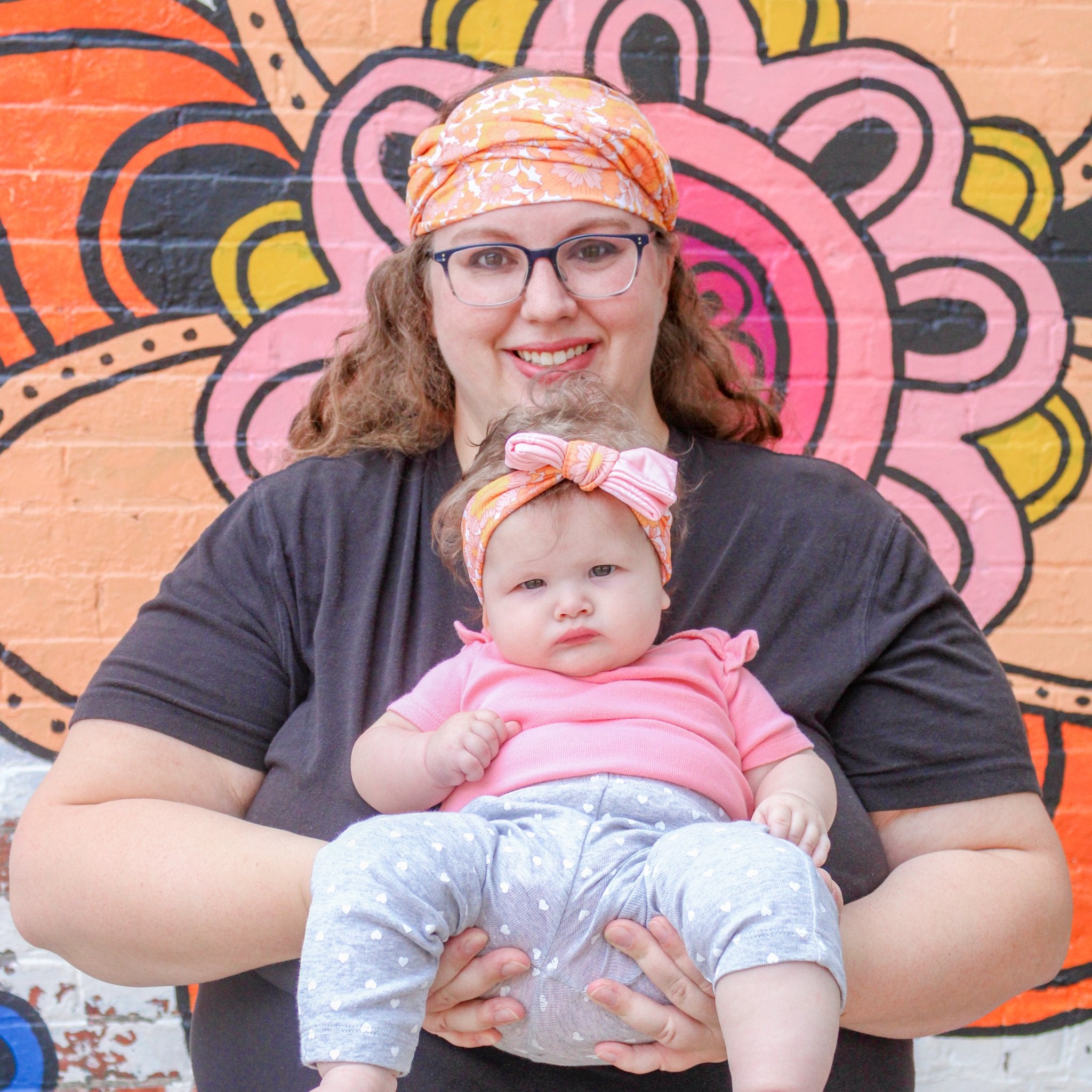 Woman holding a baby in front of a colorful mural