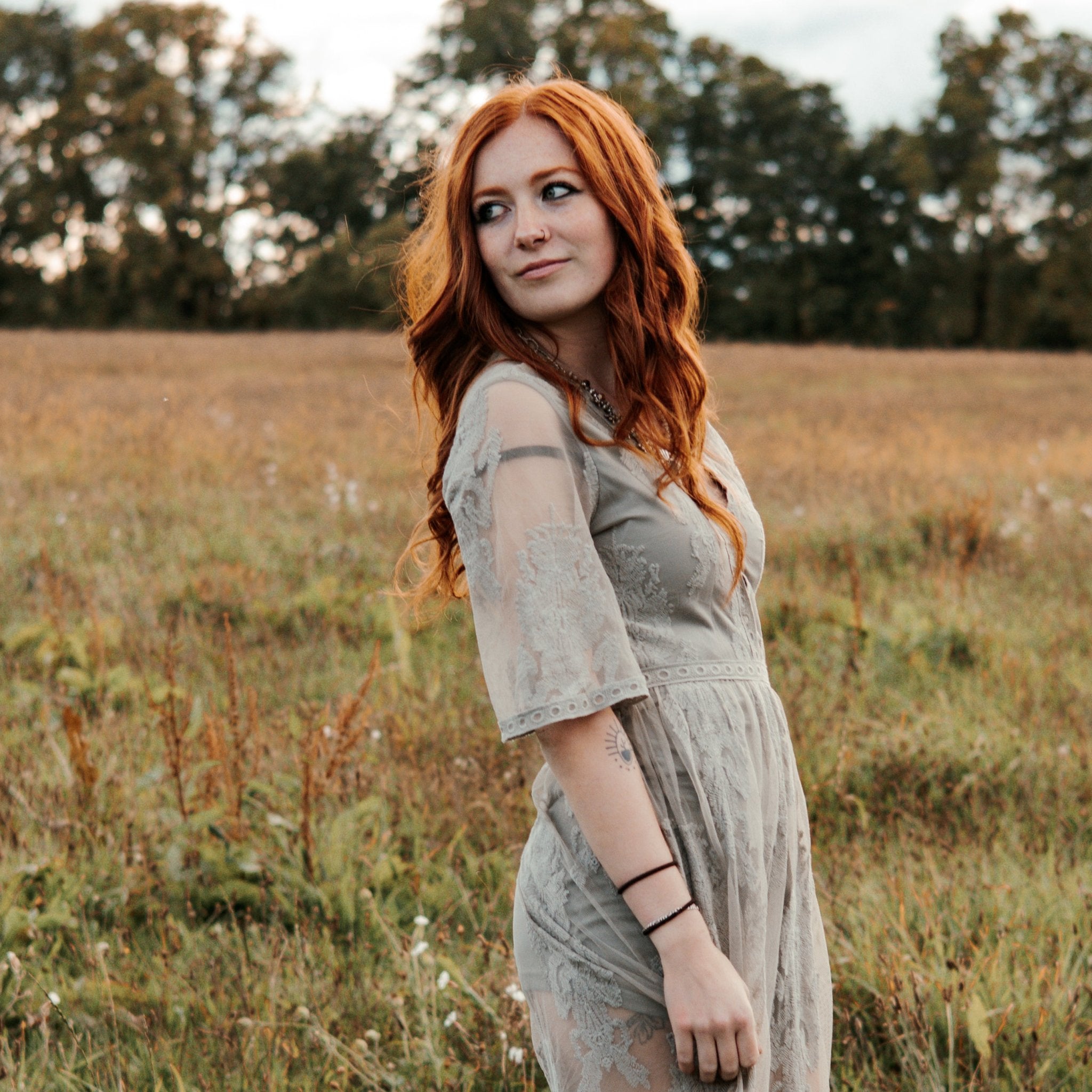 Woman with red hair standing in a field wearing a light dress.