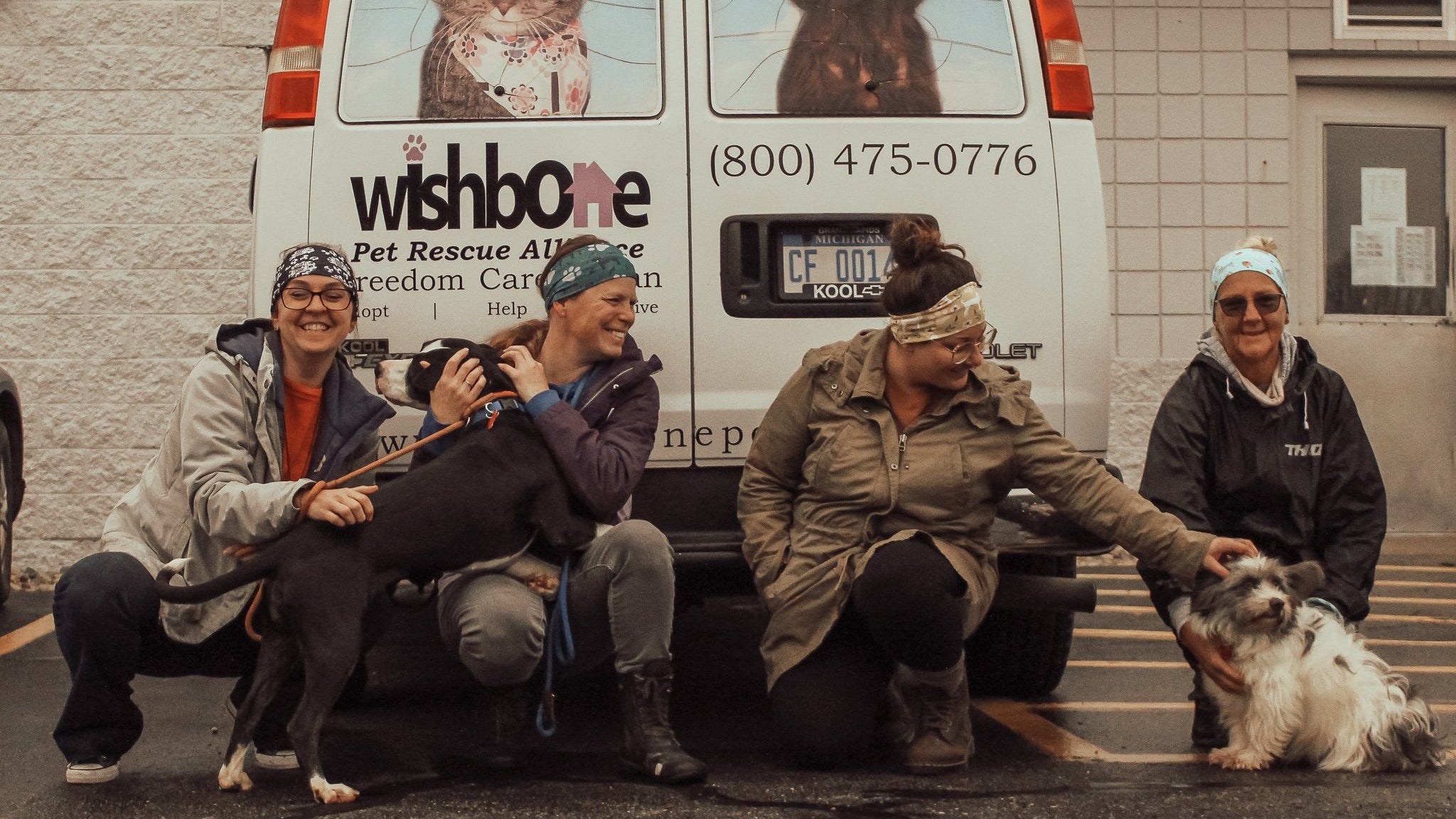 People with dogs in front of a van labeled 'wishbone Pet Rescue Alliance'
