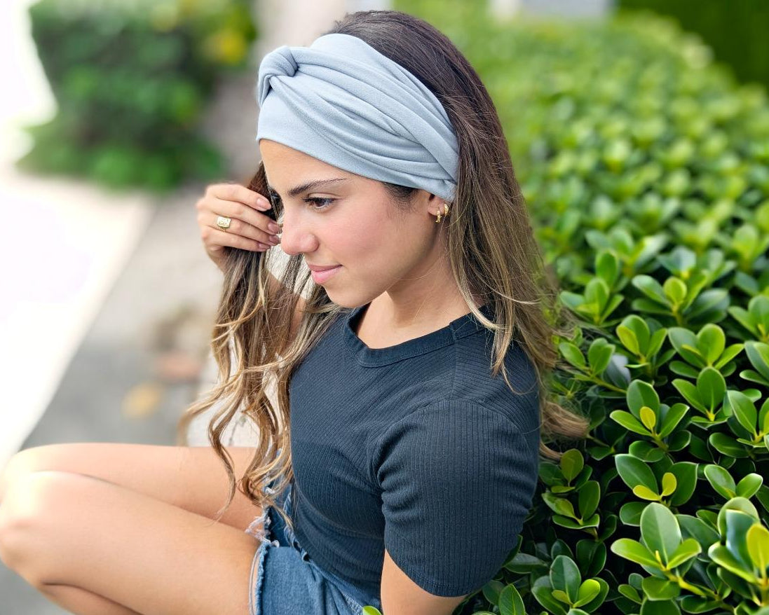 Woman wearing a gray headband sitting outdoors near green bushes